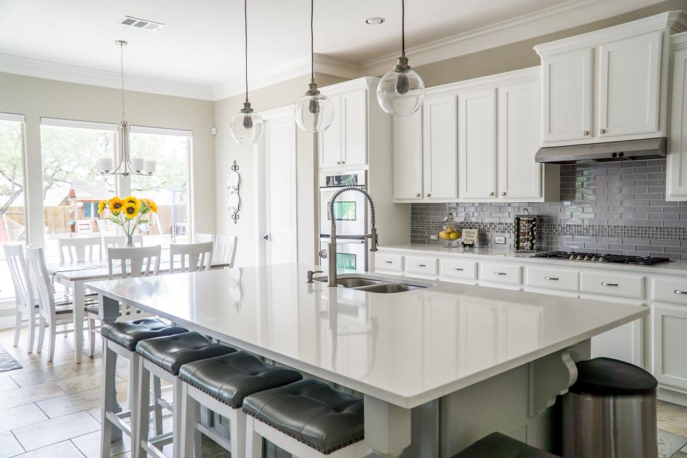 Explore the latest Kitchen Cabinet Trends with Cabinets Floors & More – dive into a world where sleek white cabinetry meets modern gray backsplash tiles, complemented by chic pendant lighting and warm wooden flooring. Perfect for your home renovation inspiration!